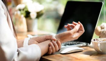 Woman holds wrist in discomfort while sitting in front of computer.