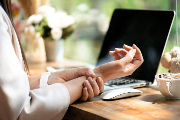 Woman holds wrist in discomfort while sitting in front of computer.