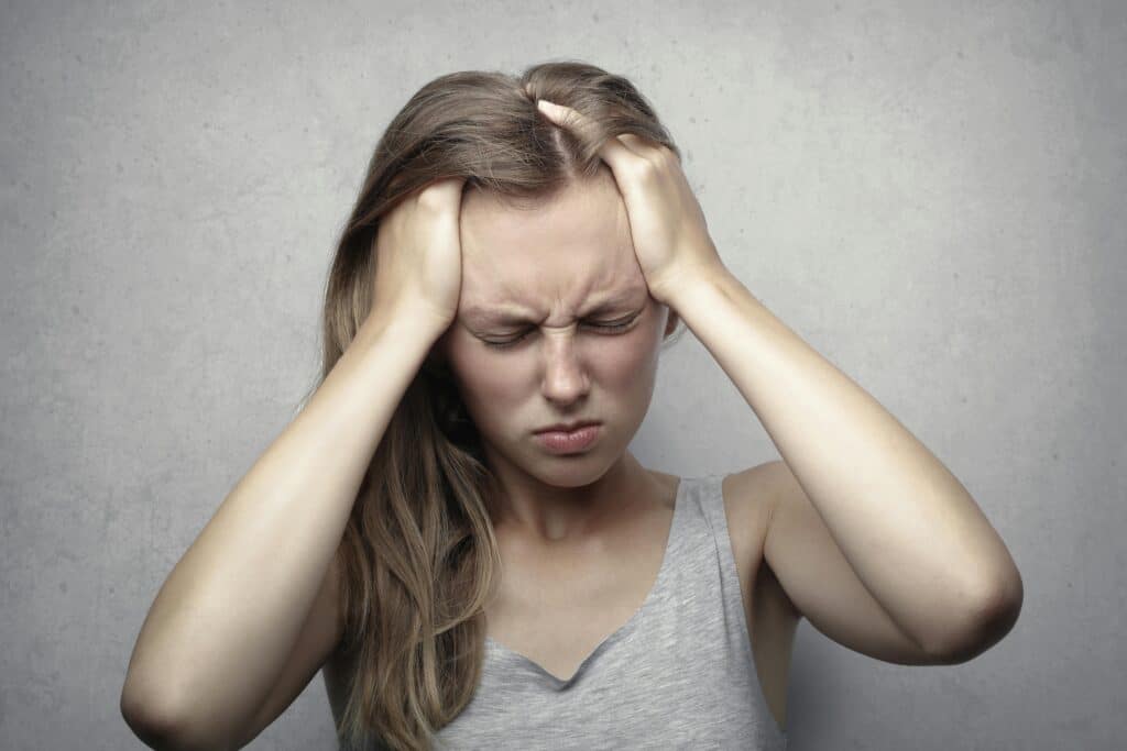 A woman touches her head with both hands, looking in pain from an extreme headache.