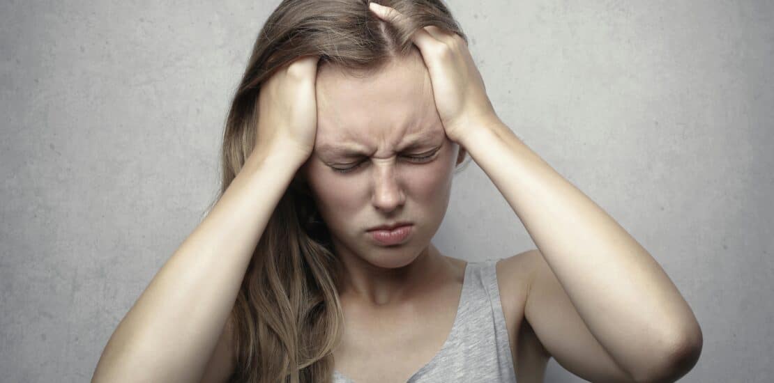 A woman touches her head with both hands, looking in pain from an extreme headache.