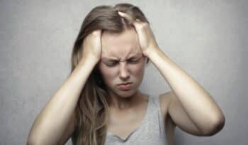 A woman touches her head with both hands, looking in pain from an extreme headache.