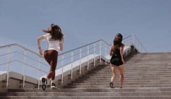 Two women are running up a set of stairs together, both appearing energetic and focused.