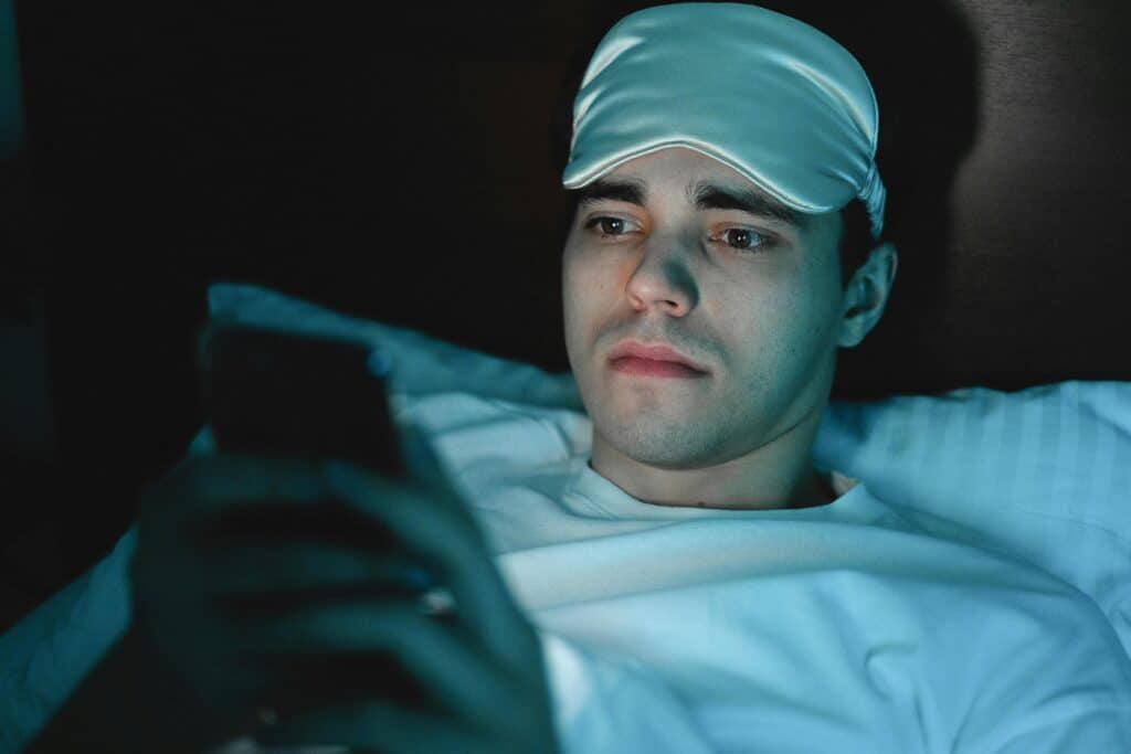 A man lying in bed in a dark room, using his phone before sleep.