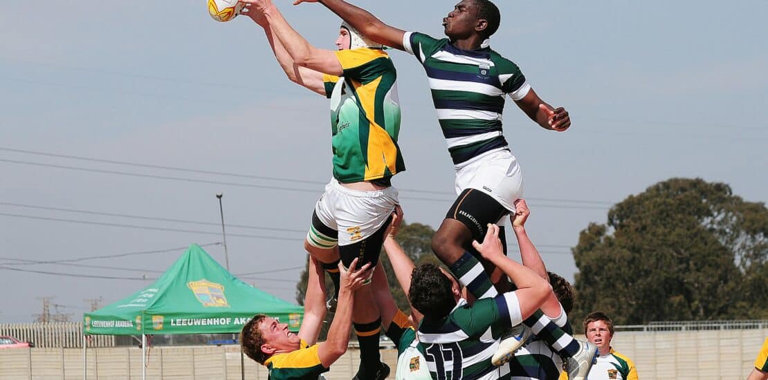 Two AFL players contesting the ball in mid-air, surrounded by four opponents, grabbing their hamstring. The intense action captures the competitive spirit of Australian football league gameplay.