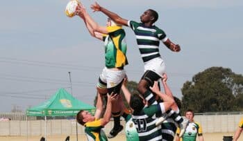 Two AFL players contesting the ball in mid-air, surrounded by four opponents, grabbing their hamstring. The intense action captures the competitive spirit of Australian football league gameplay.