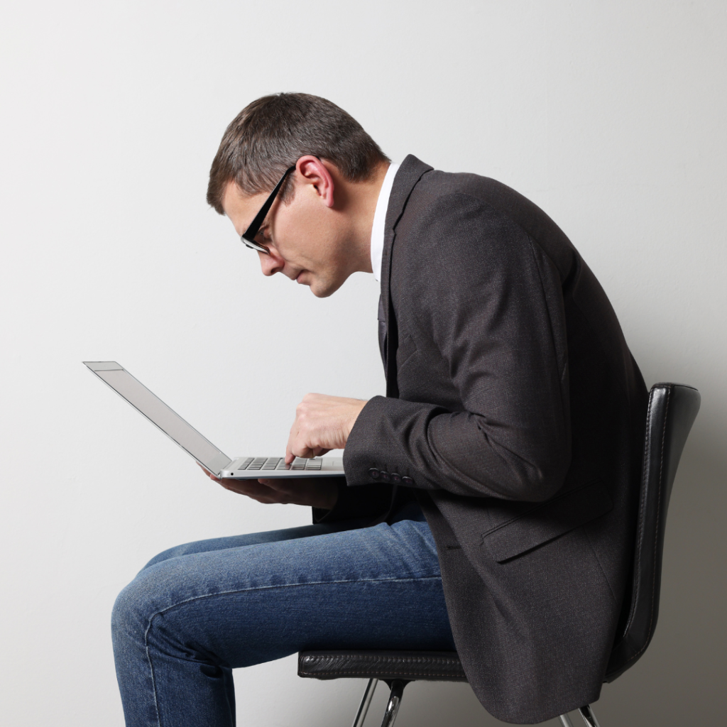 Man in corporate attire is sitting, slouching and having a very poor posture over laptop while working.