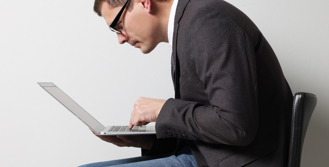 Man in corporate attire is sitting, slouching and having a very poor posture over laptop while working.