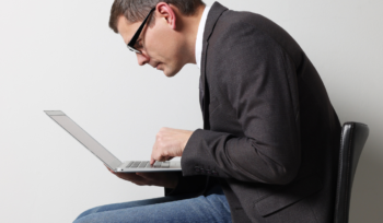 Man in corporate attire is sitting, slouching and having a very poor posture over laptop while working.