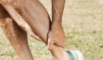 A middle-aged man wearing running shoes is seen holding his ankle in pain, likely indicating an ankle injury sustained while running.