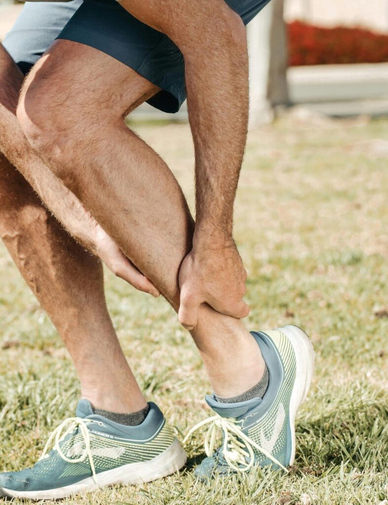 A middle-aged man wearing running shoes is seen holding his ankle in pain, likely indicating an ankle injury sustained while running.