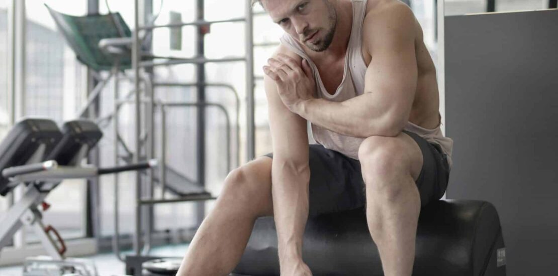 A man working out in the gym, touching his shoulder possibly due to shoulder bursitis, while exercising with a kettlebell.