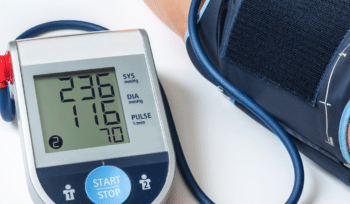 Blood pressure monitor displaying a reading of 230/116 on a patient's arm.