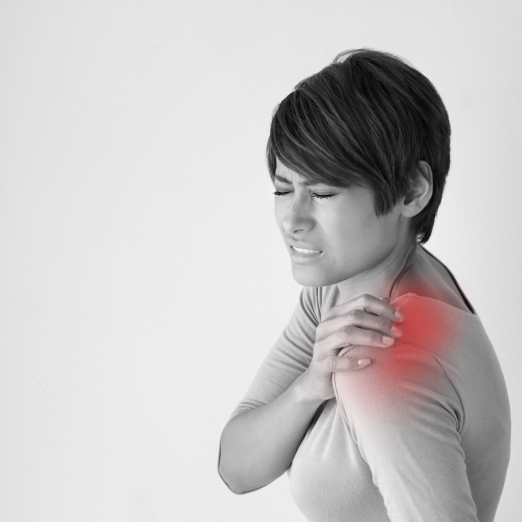 Close-up of a woman touching her shoulder with a pained expression, indicating possible frozen shoulder or shoulder discomfort.