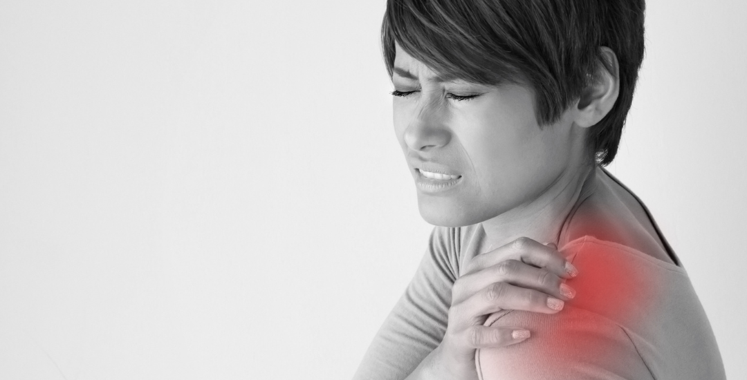 Close-up of a woman touching her shoulder with a pained expression, indicating possible frozen shoulder or shoulder discomfort.