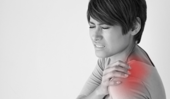 Close-up of a woman touching her shoulder with a pained expression, indicating possible frozen shoulder or shoulder discomfort.