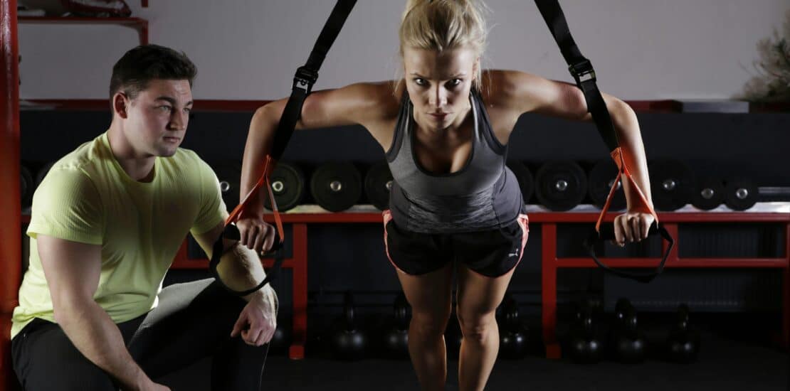 Female athlete training with a cable pulley system while her coach provides guidance and support.