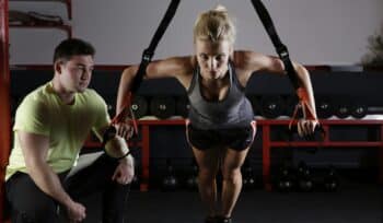 Female athlete training with a cable pulley system while her coach provides guidance and support.