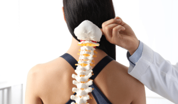 Doctor is holding an artificial spinal bone model against the woman's back, demonstrating a check for osteoporosis.