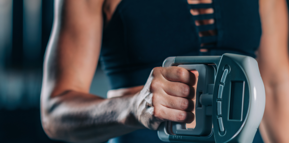 A woman with toned arms showcasing her muscles while performing a Dynamometer Hand Grip Strength Test, emphasizing her grip strength.