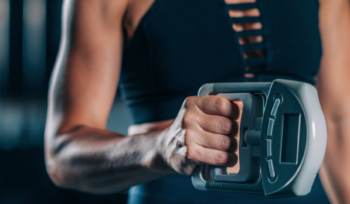 A woman with toned arms showcasing her muscles while performing a Dynamometer Hand Grip Strength Test, emphasizing her grip strength.