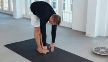 A middle-aged man stretches on a yoga mat in a gym, reaching for his toes as part of his mobility training to enhance joint health and promote flexibility.