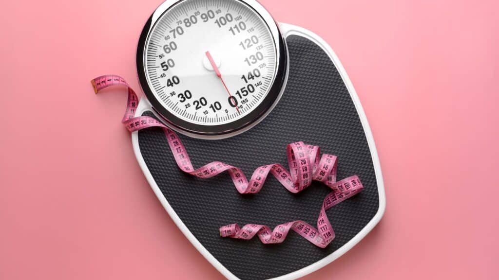 Weight scale with a tape measure lying on top, indicating positive progress in weight loss through building muscle mass.