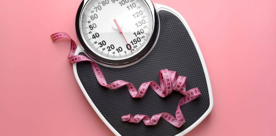 Weight scale with a tape measure lying on top, indicating positive progress in weight loss through building muscle mass.