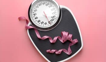 Weight scale with a tape measure lying on top, indicating positive progress in weight loss through building muscle mass.